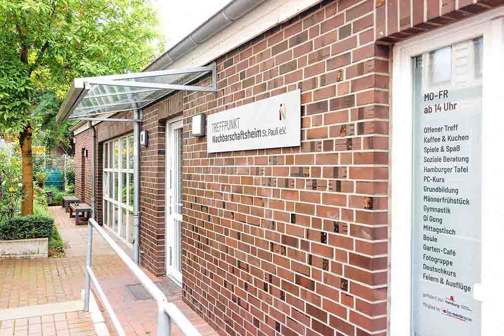 Außenansicht des Nachbarschaftsheims St. Pauli e.V. mit Eingang und Informationen zu den Angeboten wie Beratung, Freizeitaktivitäten und Kursen.
            